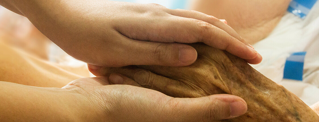 Zwei junge Hände halten die Hand eines älteren Herren.