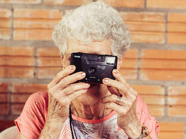 Eine ältere Dame sieht durch eine alte Kamera.