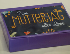 Eine lila Schachtel mit Blumenmuster mit der Aufschrift "Zum Muttertag alles Liebe"