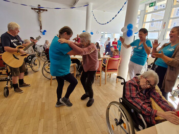 Gitarrist spielt, Seniorinnen tanzen mit Pflegepersonal, andere klatschen begeistert