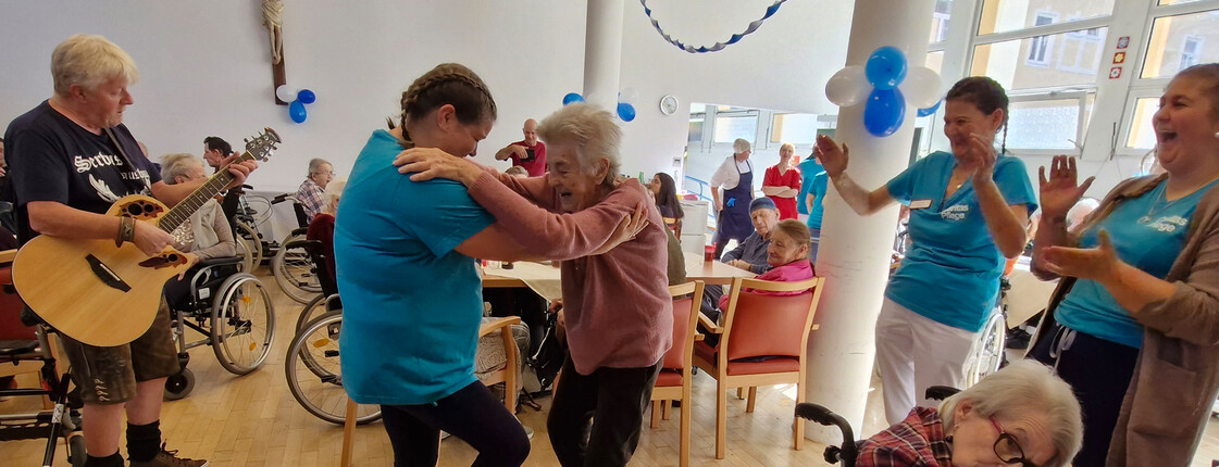 Gitarrist spielt, Seniorinnen tanzen mit Pflegepersonal, andere klatschen begeistert
