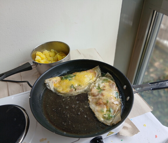 Ein tunesisches Eiergericht mit Kräutern brät in einer Pfanne neben gekochten Kartoffeln.