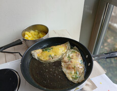 Ein tunesisches Eiergericht mit Kräutern brät in einer Pfanne neben gekochten Kartoffeln.