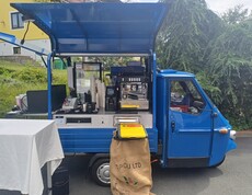 Ein blauer Kaffeewagen steht im Außenbereich des Pflegewohnhauses und ist mit einer Kaffeemaschine, Bechern und Zubehör für die Bewirtung der Gäste ausgestattet.