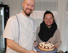 Die Hausleiterin und der Küchenchef präsentieren gemeinsam die Geburtstagstorte und lächeln in die Kamera.