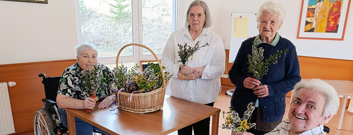Bewohner*innen sitzen zusammen und halten selbst gebundene Palmbuschen in den Händen.