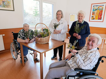Bewohner*innen sitzen zusammen und halten selbst gebundene Palmbuschen in den Händen.