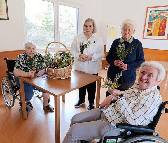 Bewohner*innen sitzen zusammen und halten selbst gebundene Palmbuschen in den Händen.