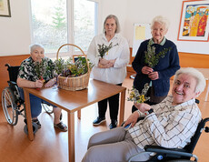 Bewohner*innen sitzen zusammen und halten selbst gebundene Palmbuschen in den Händen.