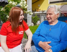 Eine Caritas Pflegerin sitzt mit einer Pensionistin im Garten.