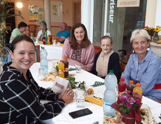 Vier Frauen, darunter Bewohnerin und Angehörige, sitzen lachend an dekoriertem Tisch beim Herbstfest.