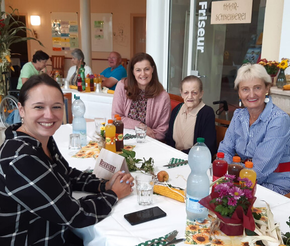 Vier Frauen, darunter Bewohnerin und Angehörige, sitzen lachend an dekoriertem Tisch beim Herbstfest.
