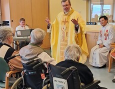 Feier eines Gottesdienstes im Pflegewohnhaus, bei dem der Weihbischof vor den sitzenden Bewohnerinnen und Bewohnern im Gemeinschaftsraum steht.