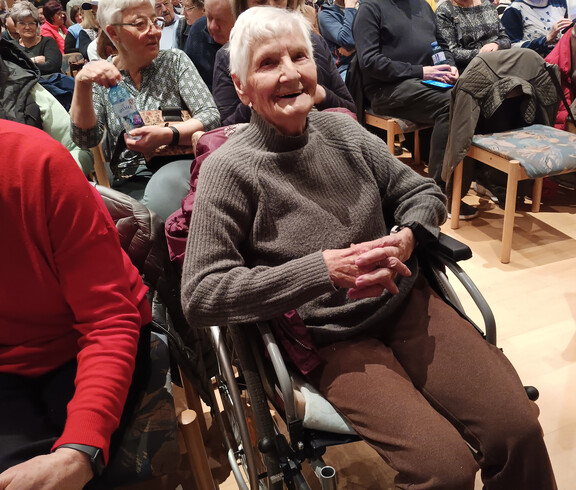 Bewohner*in des Pflegewohnhauses sitzt im Rollstuhl im Zuschauerbereich.