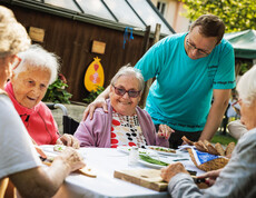 Eine Gruppe von Bewohner*innen sitzt im Garten und schneidet Schnittlauch für die gemeinsame Jause.