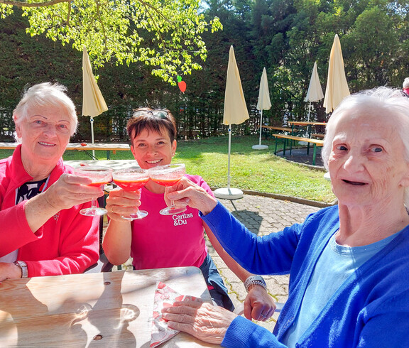 Bewohnerinnen und eine Betreuerin vom Haus Elisabeth genießen ein Erdbeergetränk beim Erdbeerfest. Sie sitzen im Freien an einen Tisch und es ist schönes Wetter