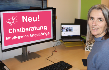 Eine Frau sitzt am Schreibstisch und lächelt in die Kamera. Am Bildschrim des Computers ist zu lesen: Neu Chatberatung für Pflegende Angehörige