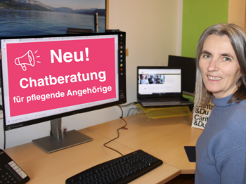 Caritas-Mitarbeiterin Irmtraud Truttenberger übernimmt die neue Chatberatung für pflegende Angehörige. Eine Frau sitzt am Schreibstisch und lächelt in die Kamera. Am Bildschrim des Computers ist zu lesen: Neu Chatberatung für Pflegende Angehörige