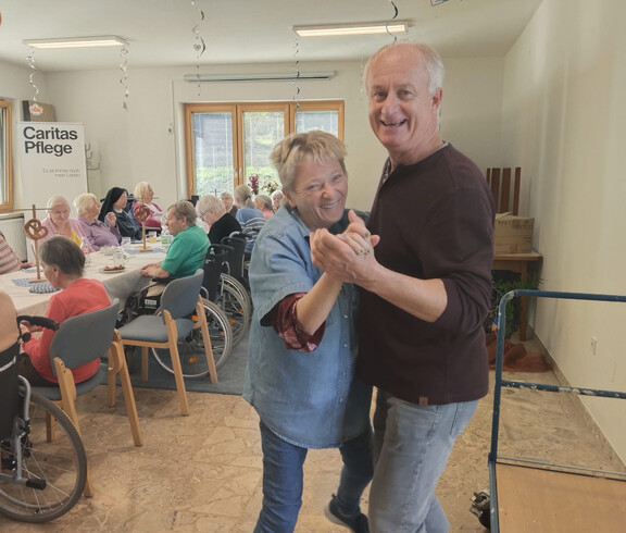 Zwei Personen tanzen lachend inmitten der feiernden Bewohnerschaft im Speisesaal.