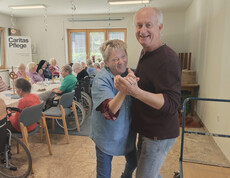 Zwei Personen tanzen lachend inmitten der feiernden Bewohnerschaft im Speisesaal.