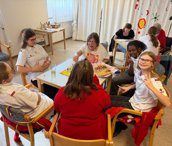 Jugendliche und Senior*innen spielen gemeinsam Brettspiele und teilen eine Platte mit Keksen.
