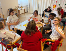 Jugendliche und Senior*innen spielen gemeinsam Brettspiele und teilen eine Platte mit Keksen.