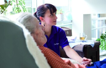 Eine Betreuerin der Caritas hält die Hand einer Seniorin