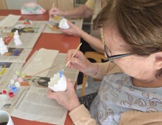 Bewohnerinnen des Pflegewohnhauses bemalen gemeinsam Keramikfiguren und gestalten farbenfrohe Osterdekorationen an einem Arbeitstisch.