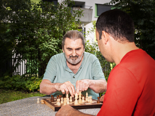 älterer Mann spielt Schach mit Caritas Mitarbeiter