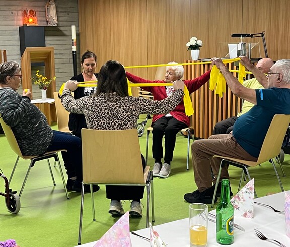 Bewohner*innen des Pflegewohnhauses sitzen in einem Stuhlkreis und führen gemeinsam mit einem Gymnastikband Bewegungsübungen zur Förderung von Mobilität und Beweglichkeit durch.