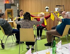 Bewohner*innen des Pflegewohnhauses sitzen in einem Stuhlkreis und führen gemeinsam mit einem Gymnastikband Bewegungsübungen zur Förderung von Mobilität und Beweglichkeit durch.
