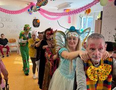 Verkleidete Bewohner*innen machen im geschmückten Raum eine Polonaise unter bunten Girlanden.