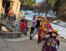 Verkleidete Bewohner*innen kommen in einer Polonaise die Rampe des Hauses hinunter, umgeben von winterlicher Landschaft.
