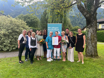 Große Freude über die E-Qalin-Auszeichnung beim gesamten Team rund um Pflegedienstleiterin Katrin Rainer (rechts im Bild mit Blumenstrauß). Mitarbeiter*innen des Pflegewohnhauses präsentieren das Zertifikat E-Qalin für das Haus.