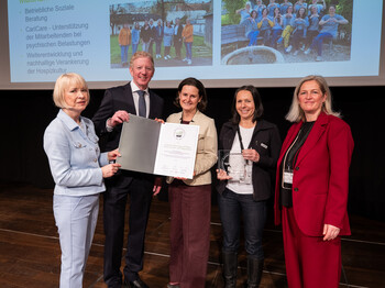Fünf Personen stehen auf einer Bühne und halten eine Urkunde in den Händen.