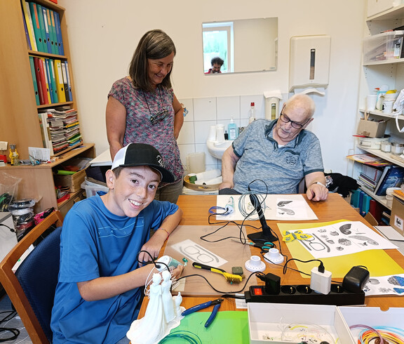 Junge und Senior arbeiten gemeinsam mit 3D-Stift an einem Tisch mit Bastelmaterial
