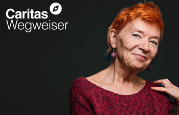 Das Porträt einer Frau ist zu sehen auf schwarzem Hintergrund. Es ist eine ältere Dame die lächelt, sie hat einen rothaarigen Kurzhaarschnitt. Links oben das Logo vom Caritas Wegweiser.