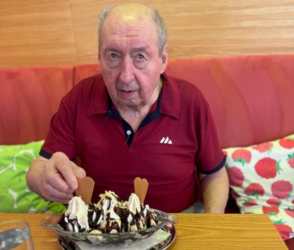 Copilot said:  Ein Bewohner sitzt am Tisch, genießt seinen Eisbecher und nimmt gerade eine Herzwaffel aus dem Eis.