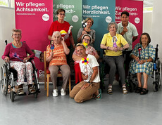 Senior*innen und Pfleger*innen präsentieren gebastelte Figuren vor bunten Caritas-Bannern.