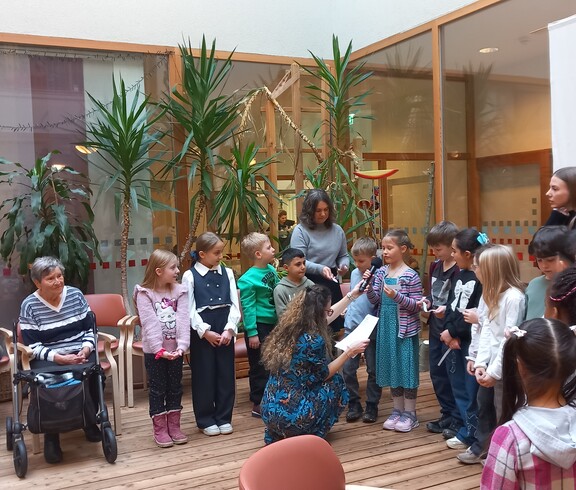 Kinder lesen anlässlich des Vorlesetages im Pflegewohnhaus den anwesenden Bewohnerinnen und Bewohnern in gemeinsamer Runde aus vorbereiteten Texten vor.
