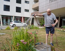 Ein Bewohner gießt mit dem Gartenschlauch die Pflanzen vor dem Eingang der Einrichtung.
