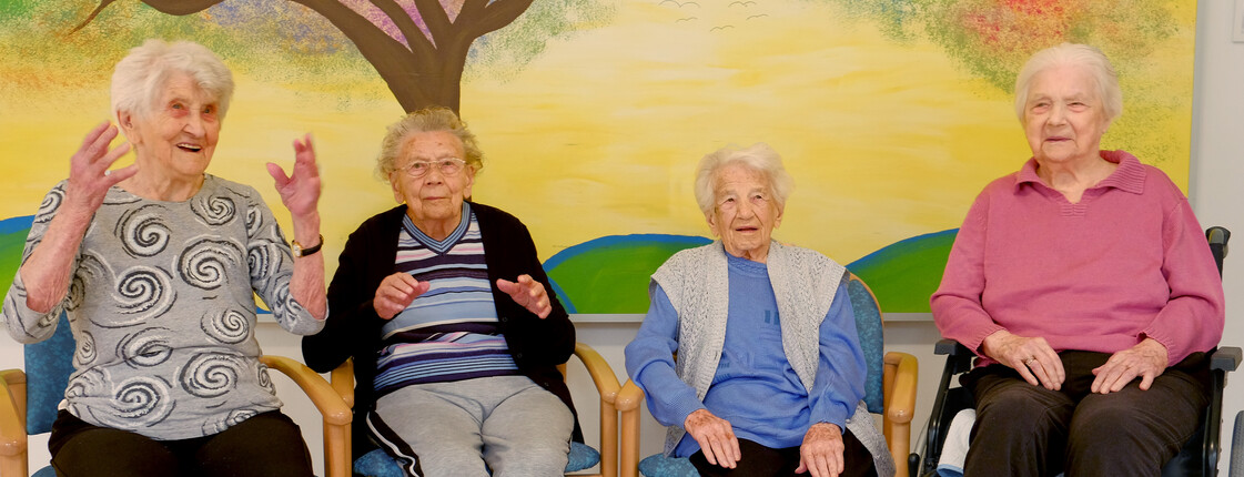 4 alte Damen sitzen und schauen in die Kamera.