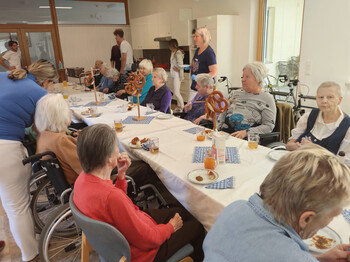Bewohner*innen sitzen gemeinsam an einer festlich gedeckten Tafel mit Brezen und Saft.