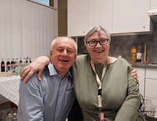 Zwei Personen sitzen eng beisammen in Küche mit Getränken im Hintergrund