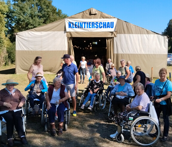 Gruppe Senior*innen mit Begleitpersonen vor Zelt mit Aufschrift „Kleintierschau“