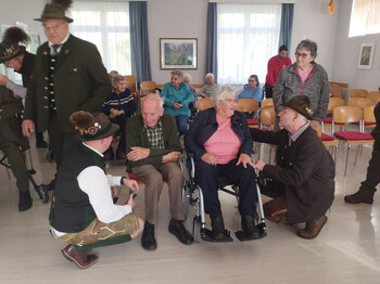 Senior*innen im Gespräch mit Jagdhornbläsern in traditioneller Tracht im Pflegewohnhaus