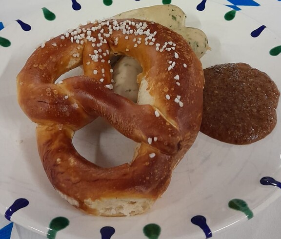 Zu sehen ist ein gedeckter Tisch mit einer traditionellen Mahlzeit: Weißwurst und Breze werden serviert, typisch für das Oktoberfest.