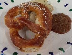 Zu sehen ist ein gedeckter Tisch mit einer traditionellen Mahlzeit: Weißwurst und Breze werden serviert, typisch für das Oktoberfest.