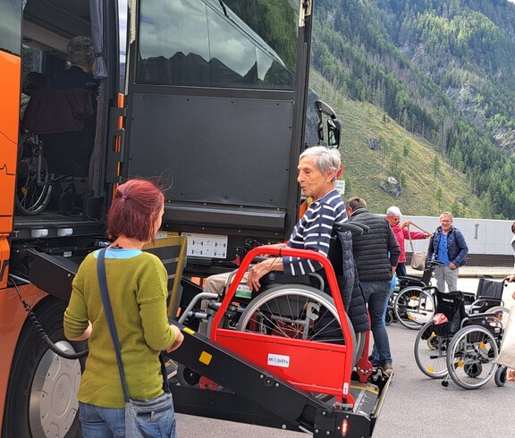 Rollstuhlnutzer*in wird mithilfe einer Hebebühne in Reisebus gehoben
