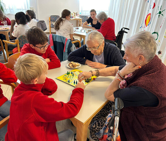 Jugendliche und Seniorinnen spielen ein Brettspiel und diskutieren über den nächsten Zug.